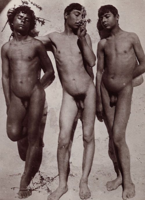 Gloeden, Wilhelm von: Drei Jungen vor einer Mauer, der mittlere an einem Bltenzweig riechend